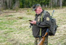 Agrivenatoria biodiversitalia, la posizione di Federcaccia Agrivenatoria biodiversitalia: cacciatore con zaino e fucile in spalla controlla telefono